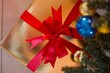 Top view of a gold gift box with a red ribbon under the Christmas tree