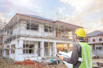 young professional engineer in protective helmet and blueprints paper at the house building construction site