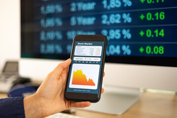 Stock market crash. Woman's hand holds a mobile phone. Droping stock chart on the screen.  PC monitor in the background. Stock market, office, trading and business concept.