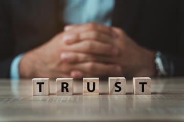 Businessman sitting behide the word trust with wooden dices on wood table. business trust concept.The concept of running a business requires trust. trust with partners.
