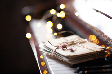 Paper snail mail letters in envelope on piano keys with dry flowers over glow Christmas lights close up. Romantic lifestyle. Valentines Day.