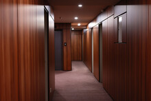 Empty Dark Interior Of The Modern Hotel Corridor, With Wood-paneled Walls, Elegant Carpets And Lighting On The Ceiling.