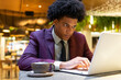 © ADDICTIVE STOCK - Serious black guy working online on netbook and smiling in cafe