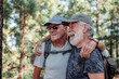 © luciano - Happy couple of old active men with hat and backpack embrace and have fun in mountain hike in the woods appreciating adventure and freedom, retired seniors and healthy lifestyle concept