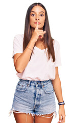 Wall Mural - Young hispanic woman wearing casual white tshirt asking to be quiet with finger on lips. silence and secret concept.