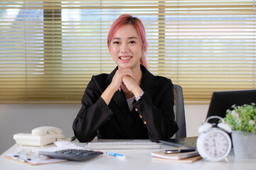 Poster - Cheerful businesswoman sitting at desk in office and looking at camera