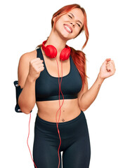 Sticker - Young redhead woman wearing gym clothes and using headphones very happy and excited doing winner gesture with arms raised, smiling and screaming for success. celebration concept.