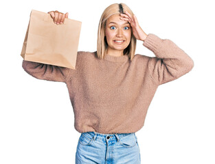 Poster - Beautiful young blonde woman holding take away paper bag stressed and frustrated with hand on head, surprised and angry face