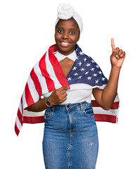 Wall Mural - Young african woman with turban holding united states flag surprised with an idea or question pointing finger with happy face, number one