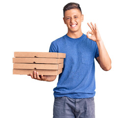 Wall Mural - Young handsome hispanic man holding delivery pizza box doing ok sign with fingers, smiling friendly gesturing excellent symbol