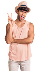 Poster - Young hispanic man wearing summer hat smiling with happy face winking at the camera doing victory sign. number two.