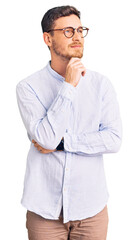 Handsome young man with bear wearing elegant business shirt and glasses with hand on chin thinking about question, pensive expression. smiling and thoughtful face. doubt concept.