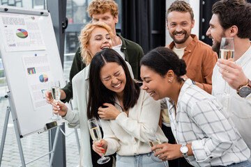 Multicultural business people with champagne laughing near flip chart in office