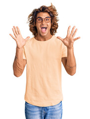 Wall Mural - Young hispanic man wearing casual clothes and glasses celebrating crazy and amazed for success with arms raised and open eyes screaming excited. winner concept