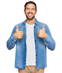 Wall Mural - Young handsome man wearing casual denim jacket success sign doing positive gesture with hand, thumbs up smiling and happy. cheerful expression and winner gesture.