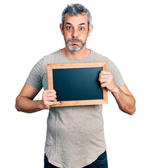 Sticker - Middle age hispanic man with grey hair holding blackboard puffing cheeks with funny face. mouth inflated with air, catching air.