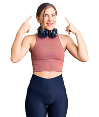 Wall Mural - Beautiful caucasian young woman wearing gym clothes and using headphones smiling pointing to head with both hands finger, great idea or thought, good memory