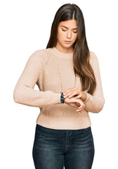 Poster - Young brunette woman wearing casual winter sweater checking the time on wrist watch, relaxed and confident