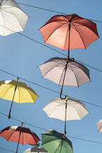 Street Scenery From Open Multi-colored Umbrellas Suspended Above Ground To Decorate City And Create Shade From Hot Summer Sun. Urban Art Object With Parasols Protecting From Sunlight Under Blue Sky