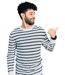 Poster - Young arab man with beard wearing casual striped sweater smiling with happy face looking and pointing to the side with thumb up.