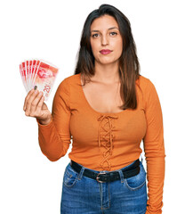 Sticker - Beautiful hispanic woman holding 20 israel shekels banknotes thinking attitude and sober expression looking self confident