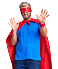 Poster - Young blond man wearing super hero custome afraid and terrified with fear expression stop gesture with hands, shouting in shock. panic concept.