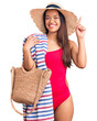 © Krakenimages.com - Young beautiful latin girl wearing swimwear and summer hat holding beach towel and bag surprised with an idea or question pointing finger with happy face, number one