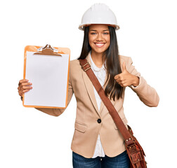 Sticker - Beautiful hispanic woman architect showing black space on clipboard smiling happy and positive, thumb up doing excellent and approval sign