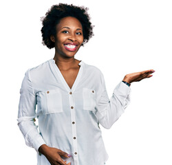 Poster - African american woman with afro hair wearing casual white t shirt smiling cheerful presenting and pointing with palm of hand looking at the camera.