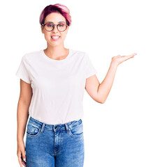 Sticker - Young beautiful woman with pink hair wearing casual clothes and glasses smiling cheerful presenting and pointing with palm of hand looking at the camera.