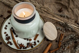 Fototapeta Mapy - Aesthetic composition of candles, anise, cinnamon sticks and coffee beans on a background of burlap, decorated with dried flowers