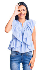 Poster - Young beautiful latin girl wearing casual clothes doing ok gesture with hand smiling, eye looking through fingers with happy face.