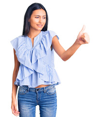 Wall Mural - Young beautiful latin girl wearing casual clothes looking proud, smiling doing thumbs up gesture to the side