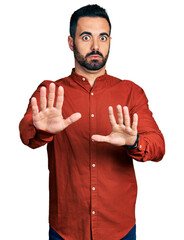 Poster - Young hispanic man with beard wearing casual shirt moving away hands palms showing refusal and denial with afraid and disgusting expression. stop and forbidden.