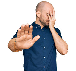 Sticker - Young hispanic man wearing casual clothes covering eyes with hands and doing stop gesture with sad and fear expression. embarrassed and negative concept.