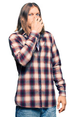 Sticker - Handsome caucasian man with long hair wearing hipster shirt smelling something stinky and disgusting, intolerable smell, holding breath with fingers on nose. bad smell