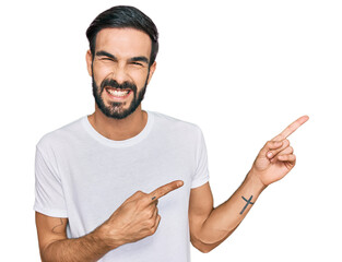 Wall Mural - Young hispanic man wearing casual white t shirt smiling and looking at the camera pointing with two hands and fingers to the side.