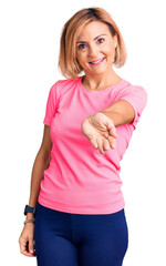 Wall Mural - Young blonde woman wearing sportswear smiling cheerful offering palm hand giving assistance and acceptance.