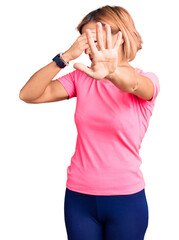 Poster - Young blonde woman wearing sportswear covering eyes with hands and doing stop gesture with sad and fear expression. embarrassed and negative concept.