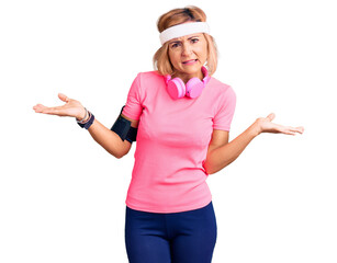 Poster - Young blonde woman wearing sportswear and headphones clueless and confused expression with arms and hands raised. doubt concept.