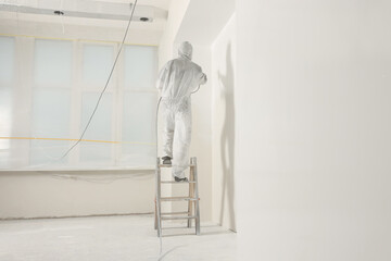 Sticker - Decorator in protective overalls painting wall with spray gun indoors