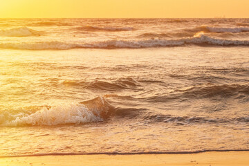 Wall Mural - Sunset above sea. Natural sunrise sky warm colors over ripple sea with small waves. Ocean water foam splash washing sandy beach at sunset.