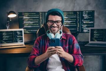 Photo of happy smiling coder dressed hat glasses headphones listen music modern device indoors workplace workstation loft