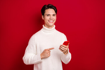 Canvas Print - Photo of positive handsome person toothy smile indicate finger hand hold telephone isolated on red color background