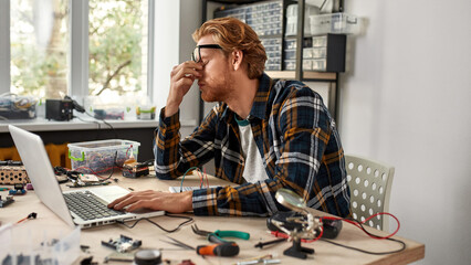 Exhausted IT technician work on laptop in office.