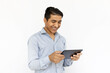 © Mangostar - Satisfied man holding tablet with both hands. Indian man in blue shirt smiling and checking tablet. Portrait, studio shot, technology concept
