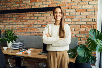 Portrait of successful female entrepreneur standing in small startup office smiling at camera