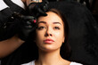 Beautiful woman undergoing procedure of permanent eyebrow makeup in tattoo salon