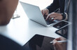 © tippapatt - Businessman in black suit sitting at table with his colleague, working on laptop computer and digital tablet in moden office, business meeting, teamwork concept, close up