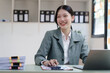 © NanSan - Pretty Asian business woman in black suit working at her office desk, with document file and paperwork. smile and looking camera